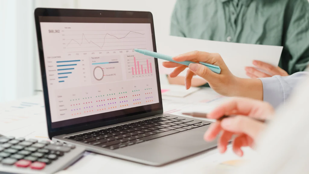A close-up view of a laptop screen displaying complex financial dashboards and charts, as an alternative lender points a light blue pen at the data to analyze a borrower's credit metrics.