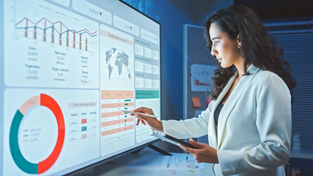 A professional female credit analyst with long curly hair using a stylus to evaluate complex financial data, charts, and a global map on a large, glowing interactive display dashboard.