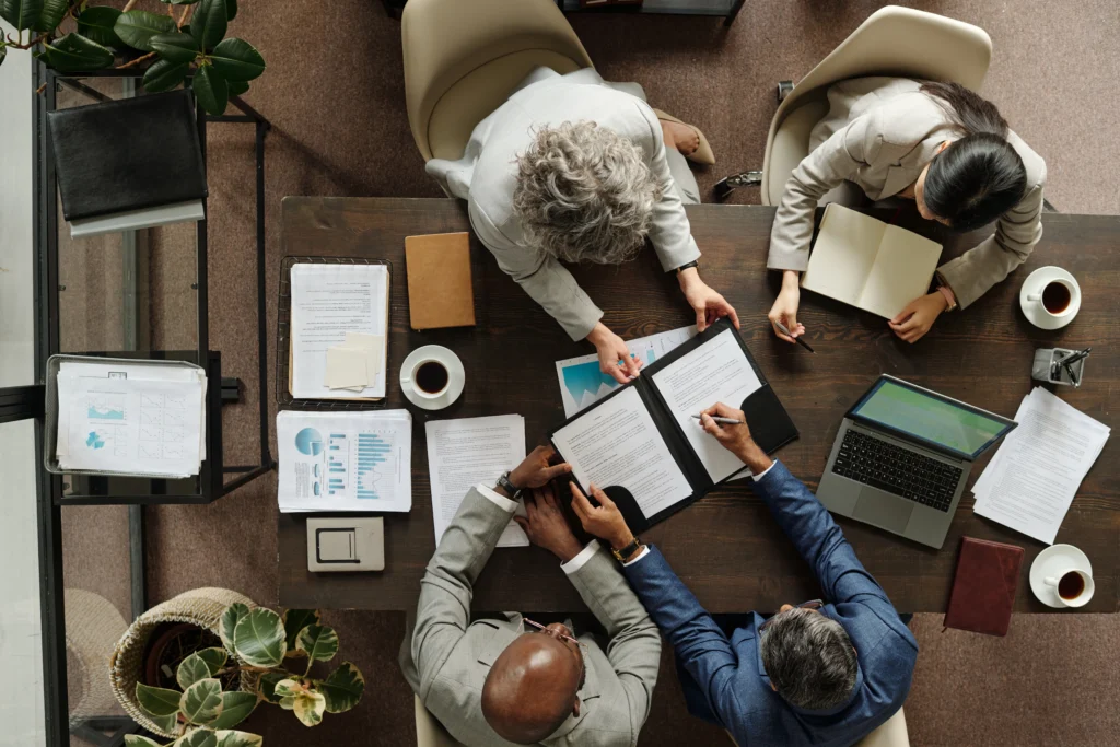 An overhead view of an experienced lending team and clients reviewing financial documents, data charts, and a laptop together at a wooden conference table, emphasizing a human-led credit decision process.